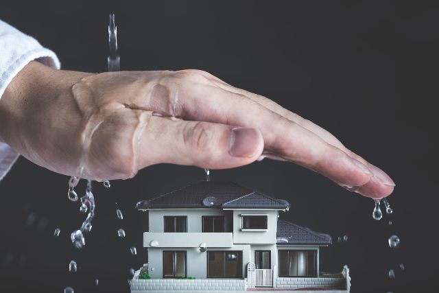 水を防ぐ人の手と家の模型